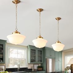 three lights hanging from the ceiling in a kitchen with green cabinets and black counter tops