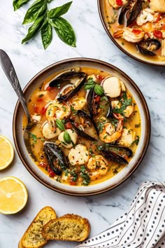 two bowls filled with seafood and mussels next to slices of lemon