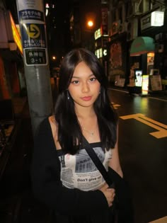 a woman standing on the side of a street at night with her arm around her chest