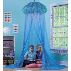 an image of two children sitting on the floor in front of a blue canopy bed