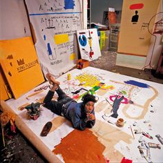 a man laying on top of a white table covered in lots of paint and paper