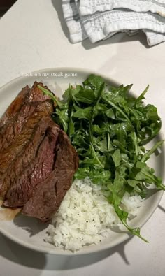 a white plate topped with steak, rice and greens