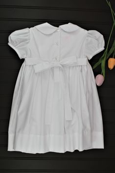 This classic dress is perfect for weddings, christenings, or blessings. The smocking on the bodice is accented with white pearls. 65% Polyester - 35% Cotton Machine wash 3 Button back closure Classic Short Sleeve Dress For Baptism, Elegant Smocked Dress With Smocked Cuffs For Baptism, Solid Color Ruffled Dress For Baptism, Classic Fitted Dress With Smocked Bodice, Fitted Wedding Dress With Smocked Cuffs, Elegant Smocked Ruffle Dress For Baptism, Elegant Baptism Dress With Smocked Back, Solid Fitted Dress For First Communion, Elegant Dress With Smocked Back For Baptism