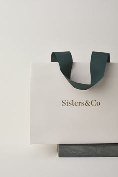 a white bag with a green ribbon hanging from it's side and the words sisters & co on it