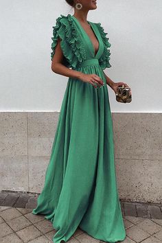 a woman in a long green dress standing next to a wall and holding a purse