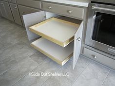 an open drawer in the middle of a kitchen with gray cabinets and white counter tops