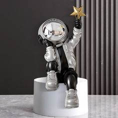 a statue of an astronaut sitting on top of a white pedestal holding a gold star