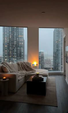 a living room filled with furniture and tall buildings in the background at sunset or dawn