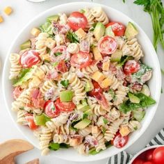 a white bowl filled with pasta salad and topped with tomatoes, lettuce and cherry tomatoes