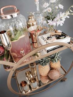 a bar cart with pineapples, books and drinks on it in front of flowers