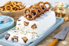 an ice cream cake with pretzels on top and other desserts in the background