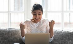 a woman sitting on a couch with her laptop in front of her and smiling at the camera