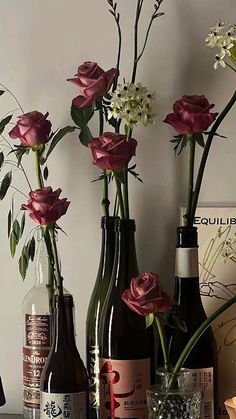 three wine bottles with flowers in them are sitting on a table next to two vases