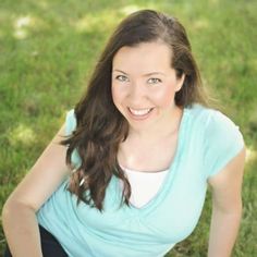 a woman sitting in the grass with her hands on her hips and looking at the camera