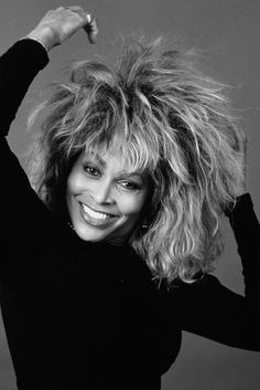 a black and white photo of a woman with her hair in the air, smiling