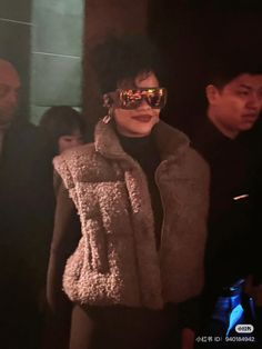 a woman wearing sunglasses and a fur coat is standing in front of some other people