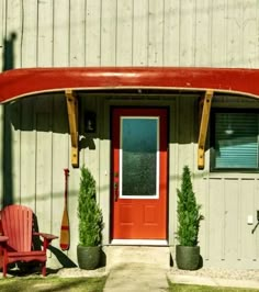 a red canoe sitting on the side of a building next to a chair and potted plants