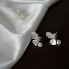 two white flower and pearl earrings sitting on top of a white satin material piece,