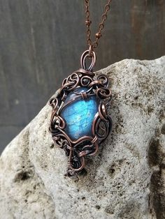 a necklace with a blue stone in the center on a chain hanging from a rock