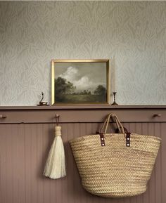 a basket hanging on the wall next to a painting and a tasseled bag