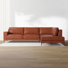 an orange leather couch sitting on top of a hard wood floor next to a white wall