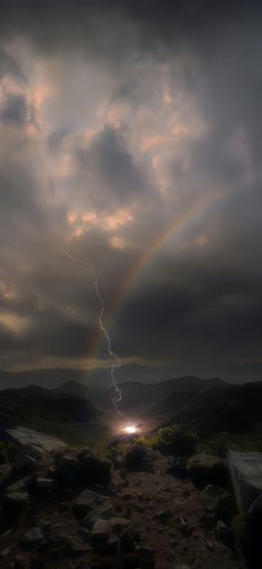 there is a rainbow in the sky and some rocks on the ground with a lightening behind it