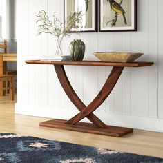 a wooden table with two pictures on the wall above it and a bowl sitting on top