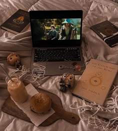 an open laptop computer sitting on top of a bed next to books and other items