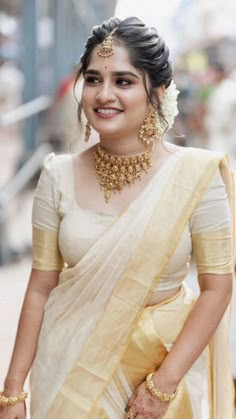 a woman in a white and yellow sari with gold jewelry on her neck, smiling at the camera