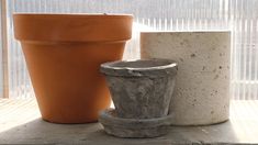 two cement pots sitting next to each other on a wooden table in front of a window