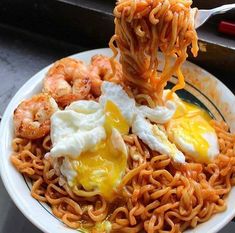 a white plate topped with noodles and shrimp next to an egg on top of it