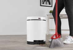 a woman is cleaning the floor with a broom and duster next to a trash can