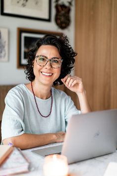 a woman sitting at a table with a laptop computer in front of her, smiling