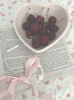 cherries in a heart shaped bowl on top of an open book