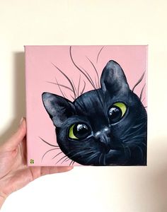 a painting of a black cat with green eyes on a pink background is being held up