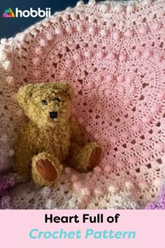 a brown teddy bear sitting on top of a crocheted blanket