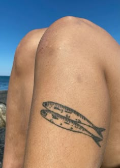 a man with a fish tattoo on his arm sitting next to the ocean and looking at the water