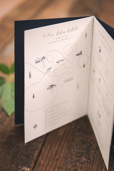 the inside of a wedding card is open on a wooden table with greenery in the background