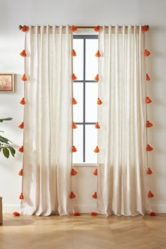 a white curtain with orange pom poms hanging from it's side in front of a window