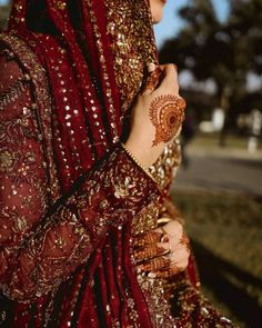 a woman wearing a red and gold bridal outfit with her hands on her chest