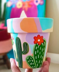 a hand holding up a flower pot with cactus designs on the outside and pink, blue, green, yellow, orange, and white colors