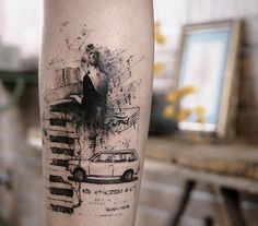 a person with a tattoo on their leg that has a car and woman in the background