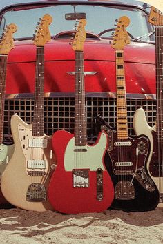 four guitars lined up in front of a red car