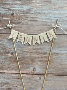 a cake topper with the name lenika on it and two wooden sticks in front of it