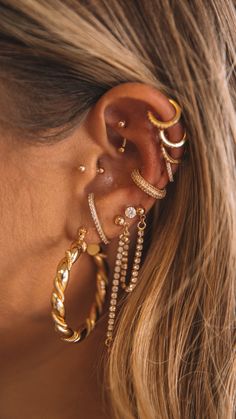 a close up of a person wearing gold ear cuffs and piercings on their ears