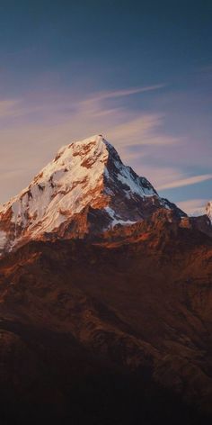 the top of a mountain with snow on it's face and clouds in the sky