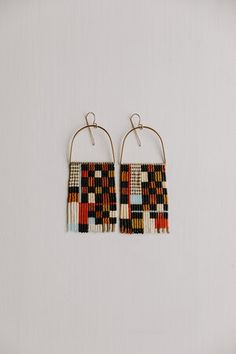 two pairs of earrings hanging from hooks on a white surface, one with multicolored beads and the other with gold hoops