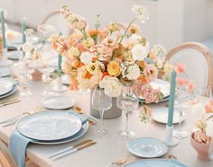 the table is set with plates, silverware and vases filled with colorful flowers