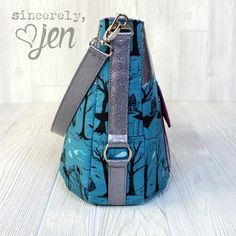 a blue purse with trees on it sitting on top of a wooden floor next to a white wall