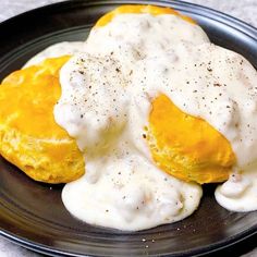 two biscuits covered in white sauce on a black plate